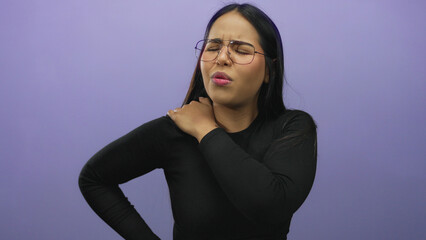 Woman in glasses massaging her shoulder in discomfort, isolated against a purple background, expressing pain relief needs.