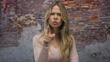 Woman pointing index finger at camera with furrowed brow in distressed brick warehouse loft;...