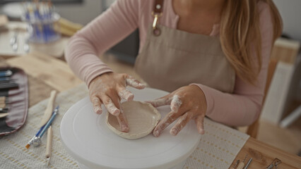 Woman shaping clay bowl with bare hands on pottery wheel in ceramics studio; creativity focus craftsmanship serenity.