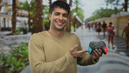 Man is showing controller in an outdoor hispanic young smiling male street gaming moment.