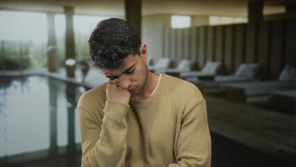 Naklejka premium Man rests hand while yawning in spa lounge beside male hispanic young guest at swimming pool feeling tired.