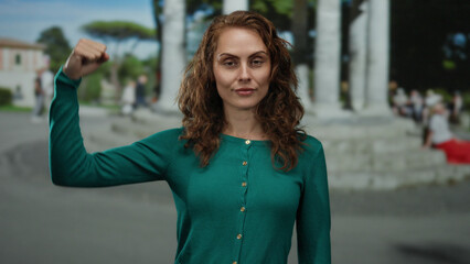 Woman confidently flexing her arm outdoors in a city setting, embodying strength and empowerment...
