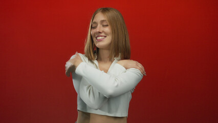 Woman smiling against a vibrant red background exudes confidence and positivity in a cropped white...