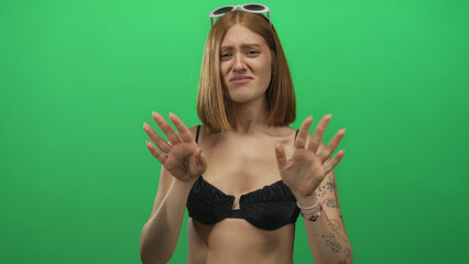 Woman expressing displeasure against green background wearing black outfit and sunglasses,...