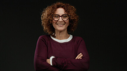 Woman smiling confidently with crossed arms against a black background, embodying elegance and...