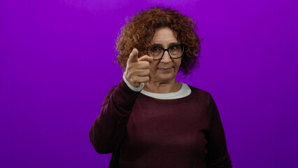 Obraz premium Middle-aged hispanic woman wearing glasses points to head against vibrant purple backdrop, conveying thoughtfulness and creativity.