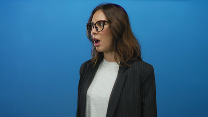 Woman wearing glasses and a blazer over a white shirt on an isolated blue background, expressing...