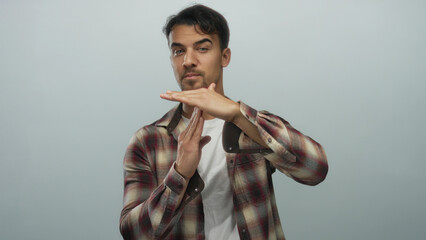 Young hispanic man gesturing timeout with hands over isolated white background in casual plaid...