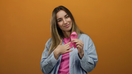 Woman smiling holding pink ribbon on vibrant orange background symbolizing health awareness and...