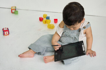 a baby sitting on the floor, holding a tablet computer in one hand and a pen in the other, surrounded by colorful blocks.