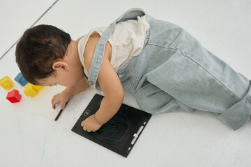 a baby laying on the floor with a tablet computer in front of them, surrounded by colorful blocks.