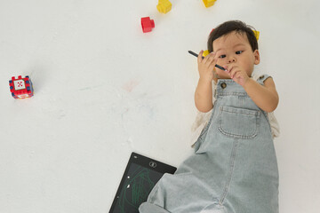 a baby sitting on the floor, holding a pencil in one hand and a tablet computer in the other....