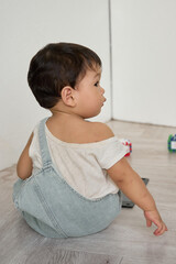 a baby sitting on the floor in front of a white wall, surrounded by toys.