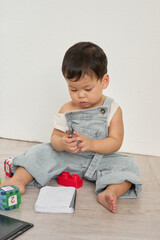 a baby sitting on the floor playing with a tablet, surrounded by books, toys, and other objects. In...