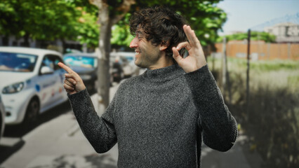 Handsome man pointing outdoors on a city street, showing an okay gesture with a cheerful...