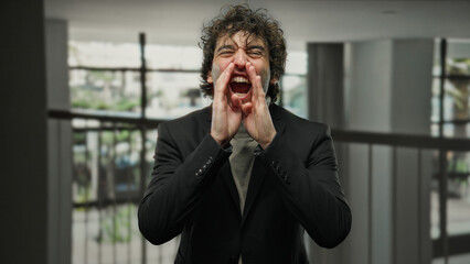 Young man shouting indoors wearing a black suit with a blurred background, conveying emotion and...