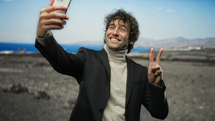 Man smiling and taking selfie at beach, wearing suit, with peace sign, capturing joyful moment with...