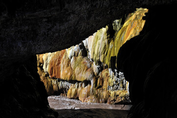 Beautiful view from the onside of the cave. Mossy rocks at the entrance to the cave. A river flowing through the entrance to the dark cave