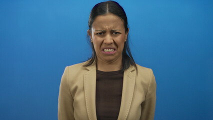 Hispanic woman makes a disgusted expression against an isolated blue background, showcasing strong emotional reaction.