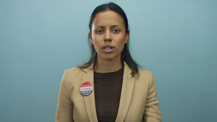 Hispanic woman with 'i voted' badge over blue background gestures for silence, emphasizing civic responsibility in the united states.