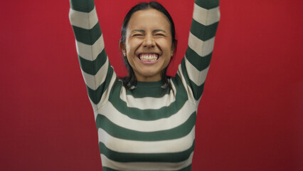 Young hispanic woman with television controller over isolated red background in an expressive...