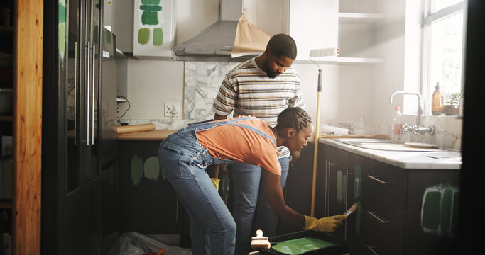 Painting, help and couple in home for renovation, diy project or remodeling together. African man, woman and paintbrush in house on kitchen cabinet for property improvement, creative upgrade or color