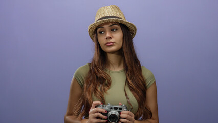 Woman holding camera against purple background wearing hat and green shirt portrays relaxed tourist...
