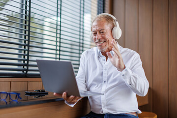 Fototapeta premium A mid aged business man in eyewear wearing headphones, holding video call on laptop. Concentrated millennial man in glasses giving online educational class lecture, consulting customer.
