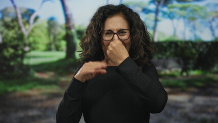 Hispanic middle-aged woman in glasses reacting with displeasure in a green park setting, showcasing...