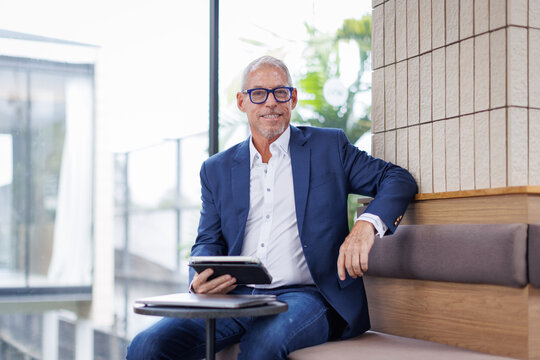  Portrait Smiling busy latin business man manager using tablet computer, happy hispanic businessman executive looking at camera holding tab working standing in office.
