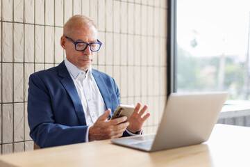 Portrait of a cheerful mid adult businessman using phone for investment plan chatting contact...