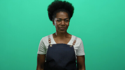 Woman wearing apron stands against bright green background radiating confidence and poise.
