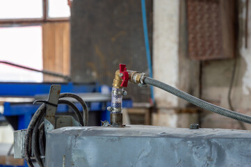 A detailed close-up shows an industrial valve connected to a hose, located in a workshop filled...