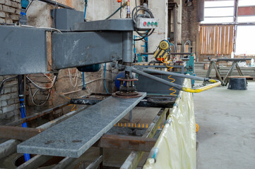 A marble cutting machine processes a large slab of stone in a workshop as sunlight filters through large windows, indicating afternoon