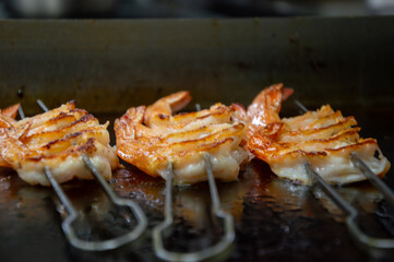Fresh shrimp skewers are sizzling on the grill, releasing appetizing aromas while being perfectly cooked in a bustling kitchen
