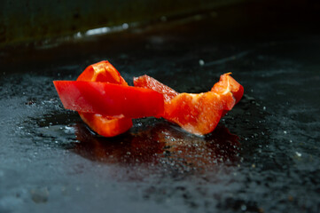 Bright red bell pepper slices are arranged in an artistic manner on a glossy black surface,...
