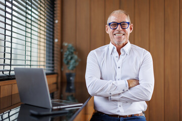 Successful middle aged businessman in shirt posing with crossed hands, looking away and smiling,...