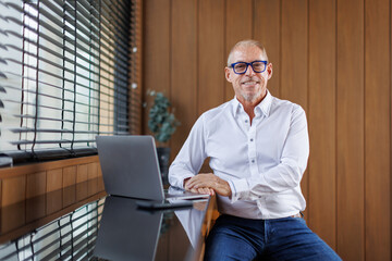 Successful middle aged businessman in shirt posing with crossed hands, looking away and smiling,...