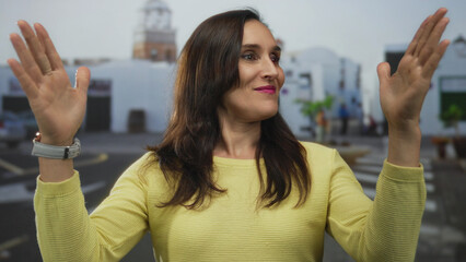 Young hispanic woman stands in a historic outdoor plaza and makes a large size gesture with hands;...