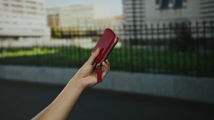 Hand holding red wallet in urban street background, indicating shopping or travel in a city...