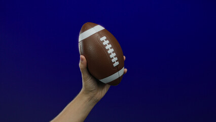 Man holding brown football against vibrant blue background showcasing sports theme and strength of grip.