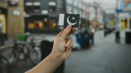 Man holding embroidered pakistan flag in hand outdoors on city street, showcasing national pride...