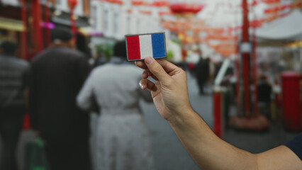 Man holding french flag patch on busy street with colorful decorations and people walking in...
