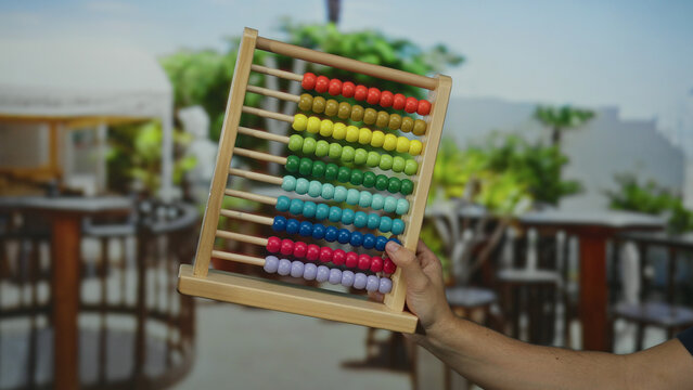 Man holding colorful abacus on city terrace restaurant creating a playful urban outdoor educational theme with vibrant atmosphere and blurred background.