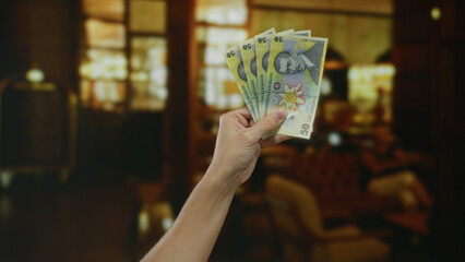 Man holding romanian lei banknotes inside a cozy coffee shop with warm lighting in a restaurant...