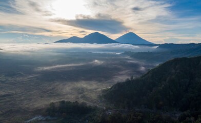 Fototapeta premium Sunrise over Mount Batur and Mount Agung, volcanoes in Bali, Indonesia. The landscape is filled with mist and clouds in the early morning light.