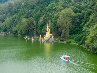 Naklejka premium Tourists enjoy a boat ride on Danau Batur, near golden statues of Hindu deities, in Bali, Indonesia. Visitors explore the scenic lake and cultural landmarks. Dewi Danu, Bali, Indonesia