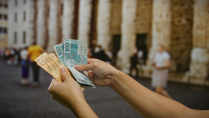 Man holding brazilian reais outdoors in an urban street, showcasing currency exchange in a bustling...
