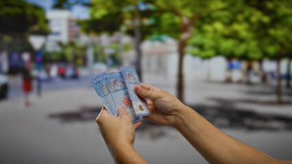Man counting malaysian ringgit banknotes outdoors against an urban city street backdrop,...