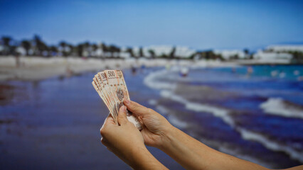 Man holding mexican pesos on a beach, symbolizing investment opportunity and leisure under the...